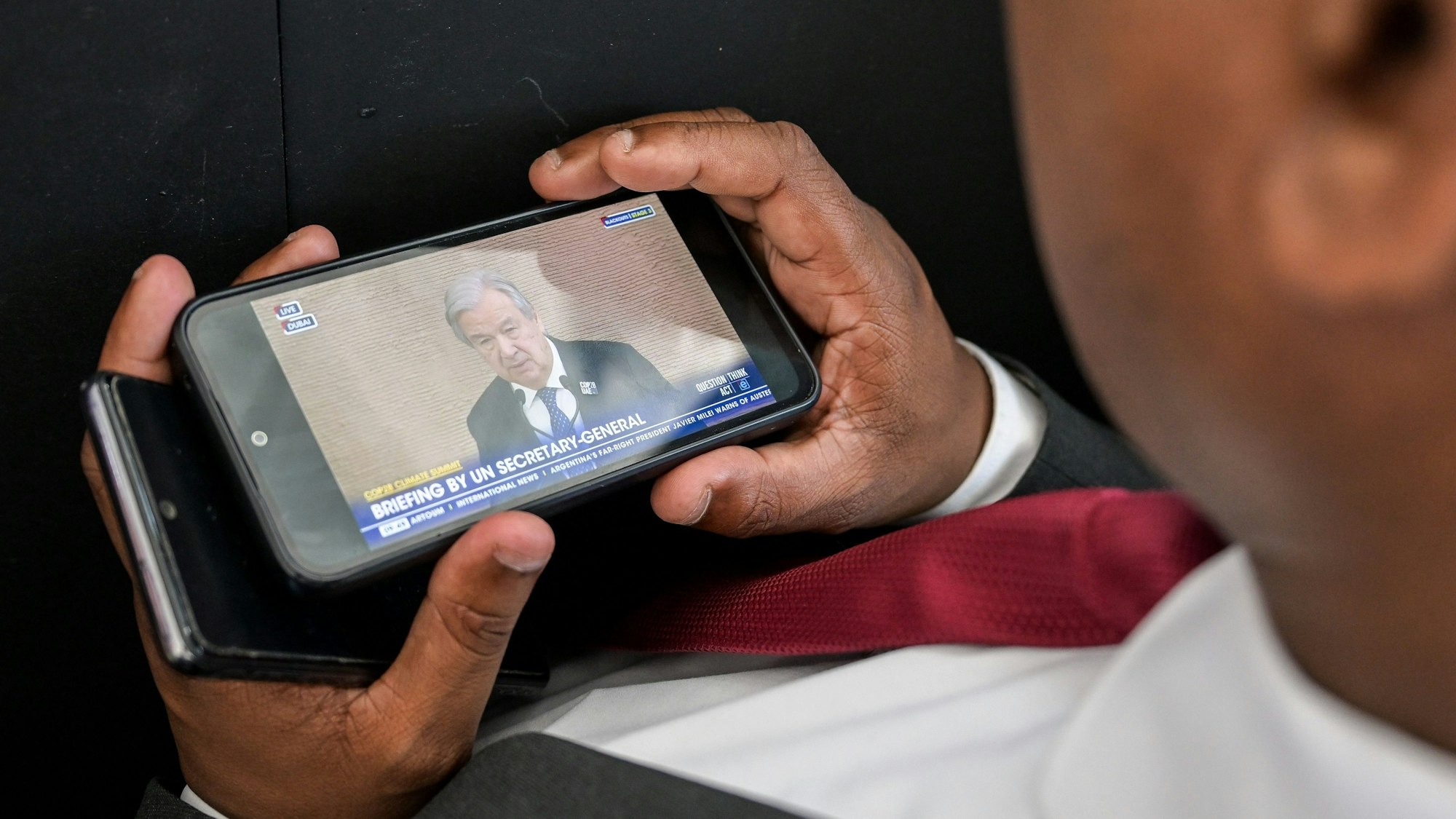 Ein Mann verfolgt auf einem Smartphone die Pressekonferenz von UN-Generalsekretär Antonio Guterres.