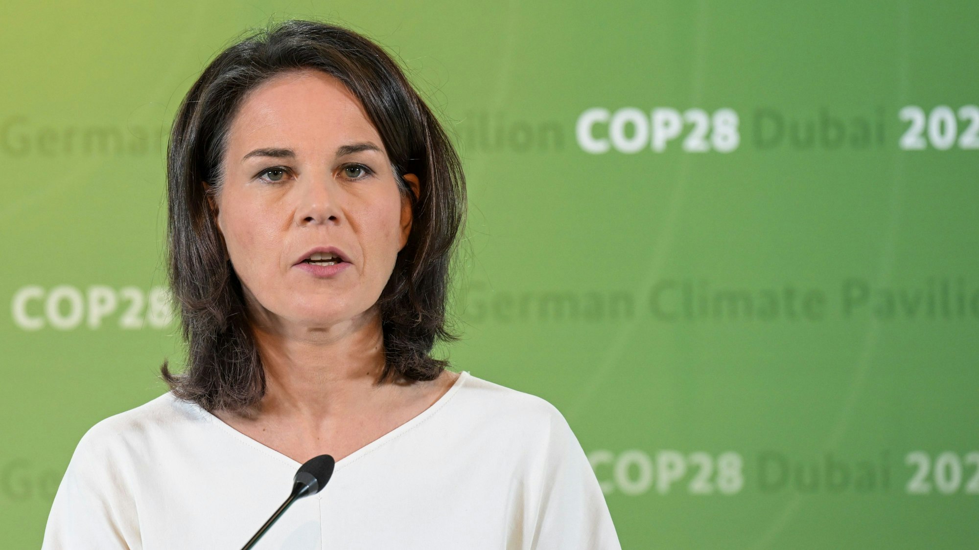 Annalena Baerbock (Bündnis 90 / Die Grünen) steht vor einer grünen Wand mit dem sich wiederholenden Aufdruck „German Climate Pavilion COP28 Dubai 2023“.
