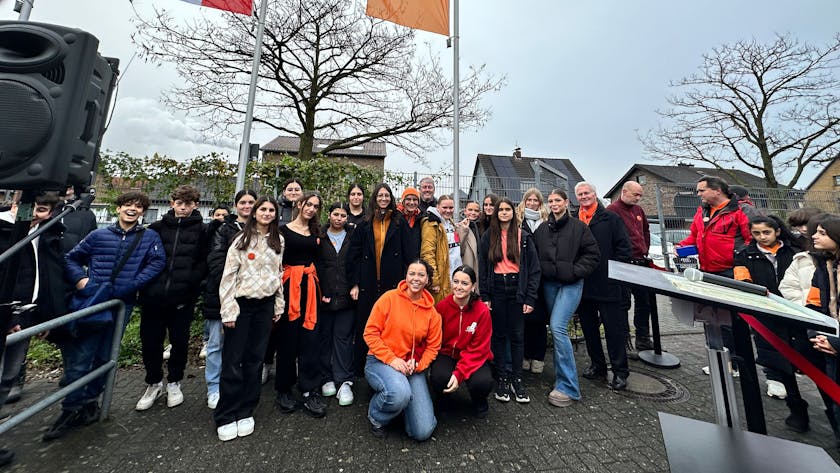 Gruppenfoto mit Schülern und Bezirksbürgermeister Manfred Giesen, die orangene Fahne und die mit dem Kölner Wappen im Hintergrund zu sehen.