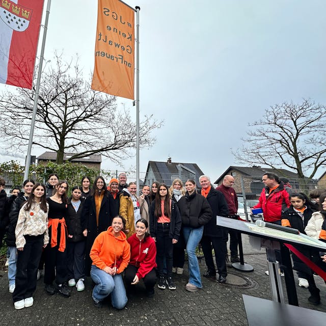 Gruppenfoto mit Schülern und Bezirksbürgermeister Manfred Giesen, die orangene Fahne und die mit dem Kölner Wappen im Hintergrund zu sehen.