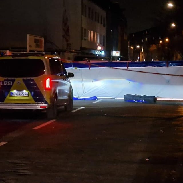 Ein Polizeiwagen steht in der Nacht vor einer Absperrung auf der Vitalisstraße in Köln.