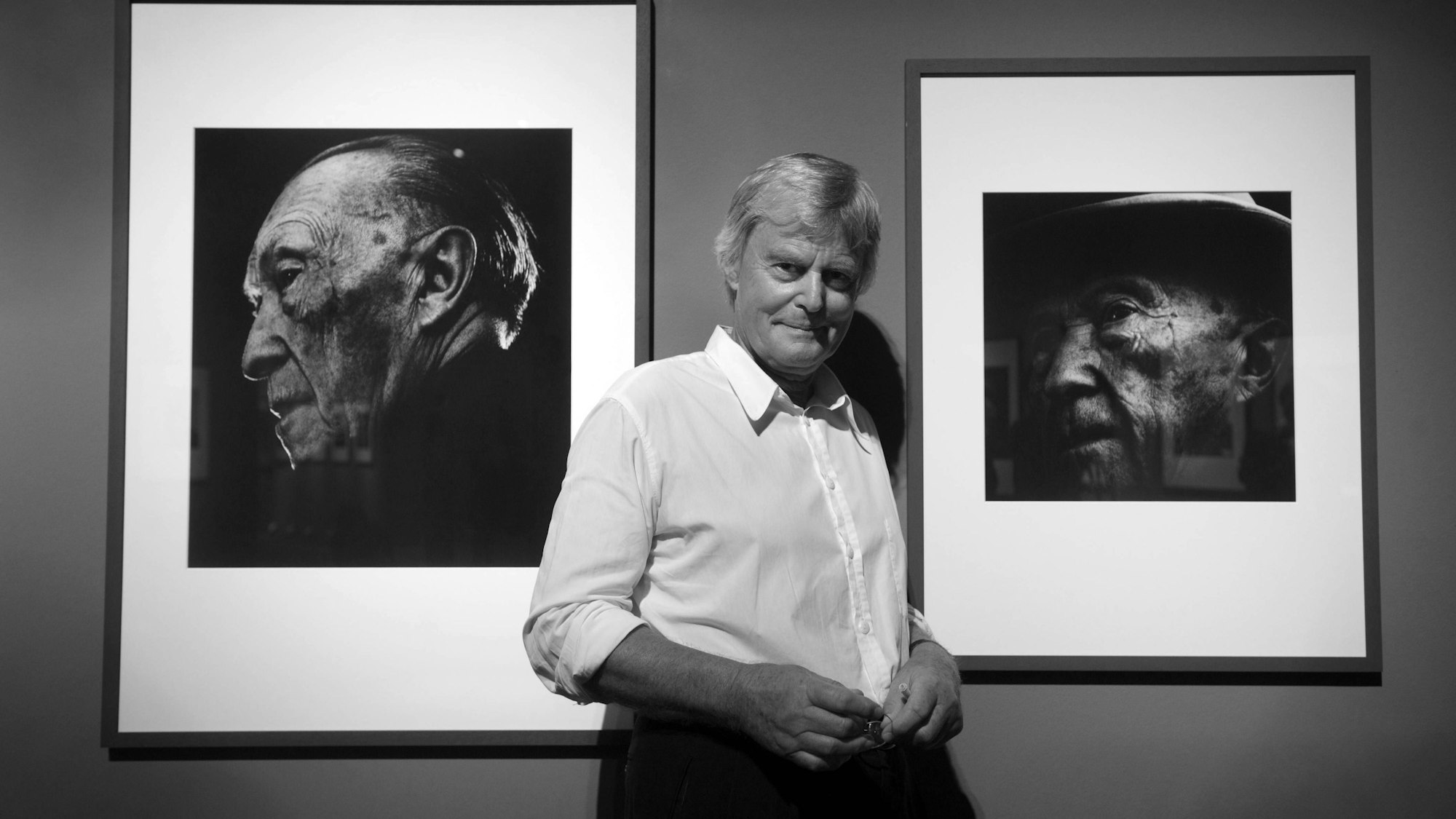 Konrad Rufus Müller posiert zwischen zwei Adenauer-Fotografien an der Wand.