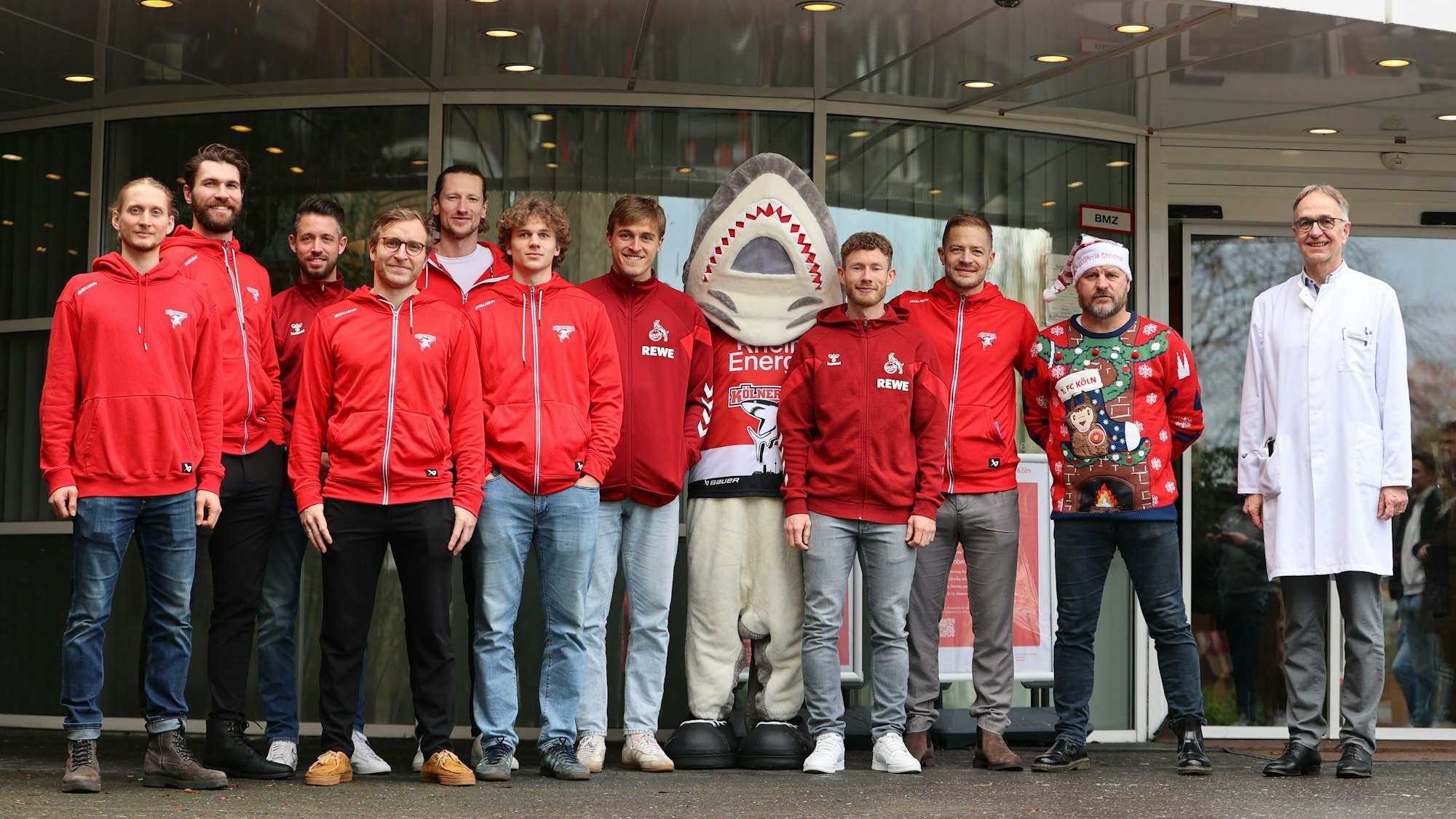 Stars des 1. FC Köln und der Haie posieren vor dem Kinderkrankenhaus für ein Gruppenfoto.