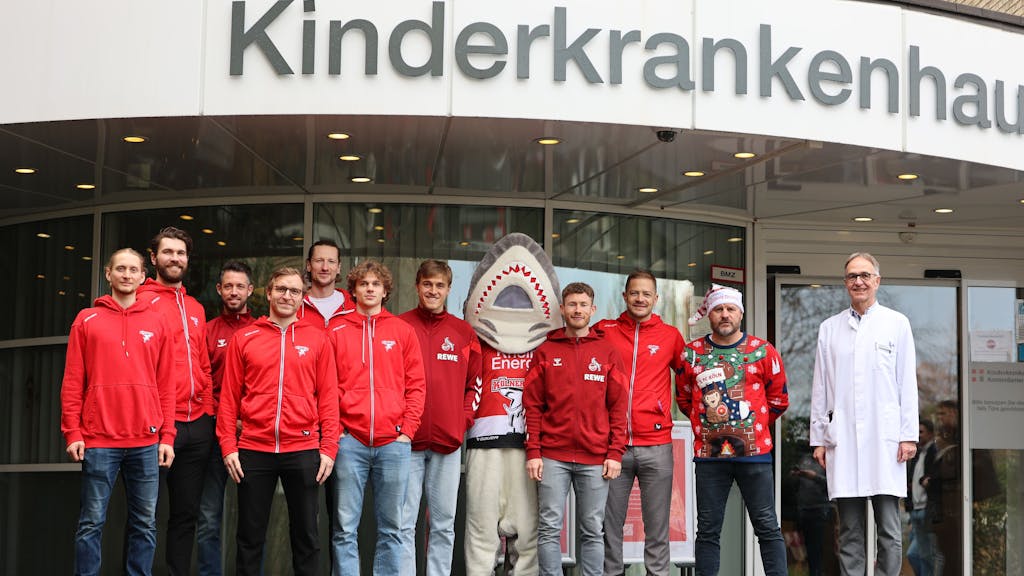 Stars des 1. FC Köln und der Haie posieren vor dem Kinderkrankenhaus für ein Gruppenfoto.