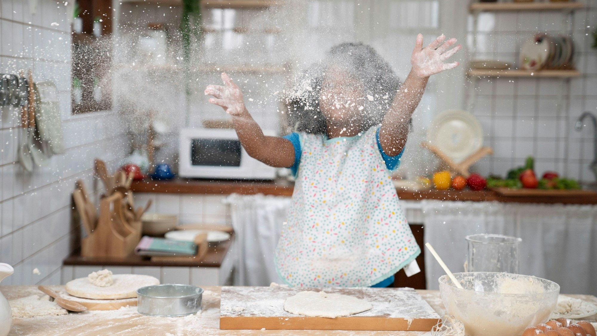 Ein kleines Mädchen wirft beim Backen Mehl in die Luft.