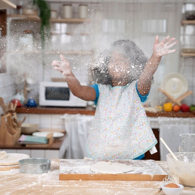 Ein kleines Mädchen wirft beim Backen Mehl in die Luft.&nbsp;
