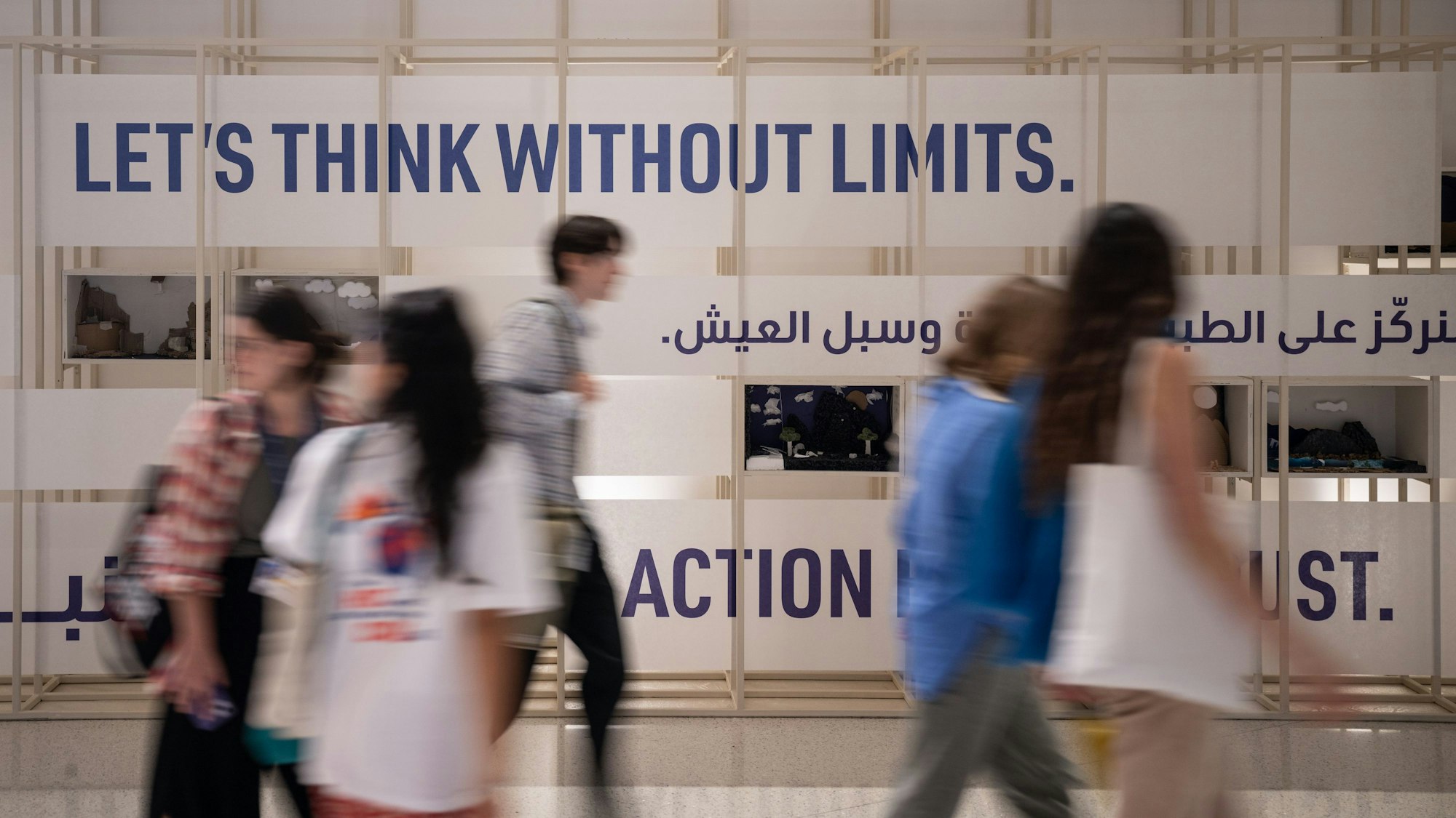 Menschen gehen vor einer Wand mit der Aufschrift «Let's Think Without Limits» (Denken wir ohne Grenzen) auf dem Gelände des UN-Klimagipfels COP28.