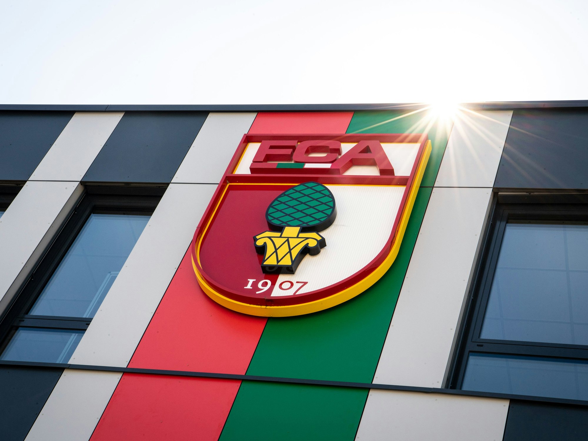 Das Vereinslogo des FC Augsburg, ein Wappen mit der Aufschrift FCA und der Abbildung einer Zirbelnuss, ist auf der Fassade der Geschäftsstelle des FC Augsburg an der WWK-Arena zu sehen.