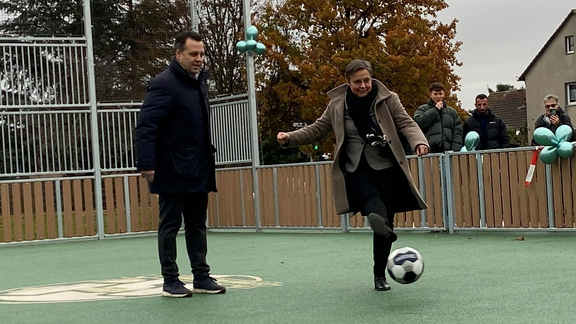 Auf einem Tartan-Platz kickt Schulleiterin Karin Bossant unter den Augen des Bürgermeisters Sacha Reichelt einen Fußball.