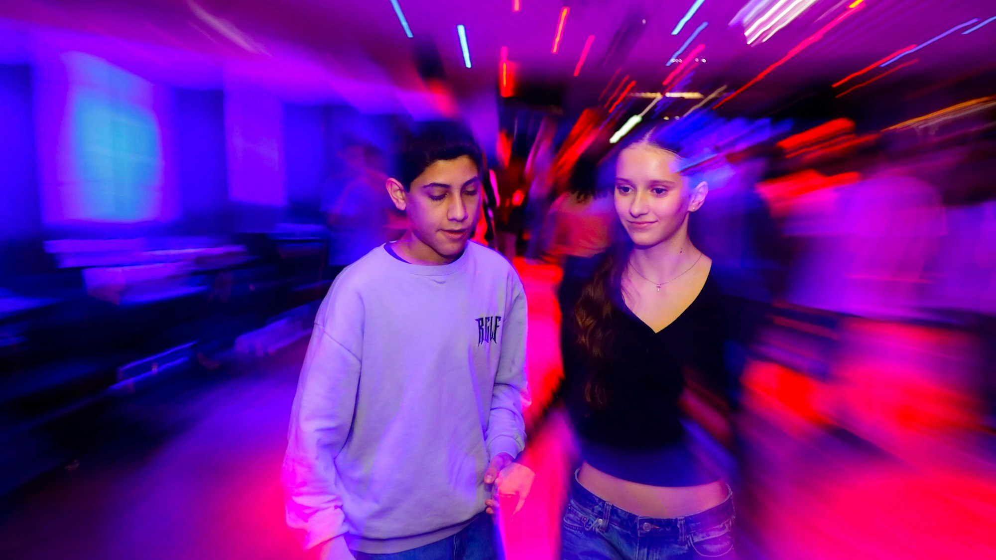 Alessia und Omid tanzen, eingetaucht in buntes Disco-Licht.