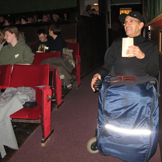 Ein Mann im Rollstuhl hat im Kino-Saal im Parkett seinen Platz eingenommen.