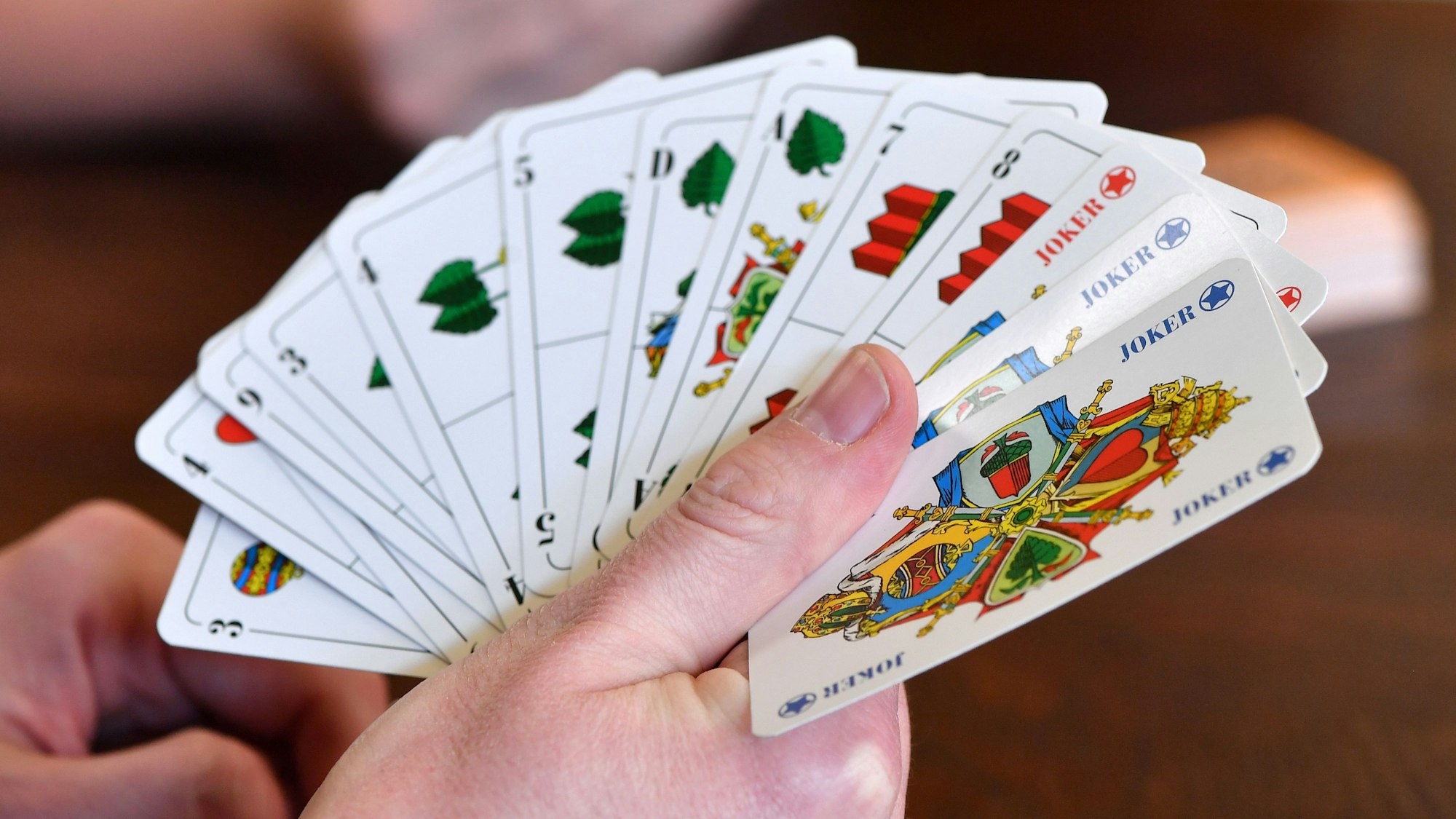 Kartenspieler spielen mit einem Rommé-Blatt mit deutschem Bild.