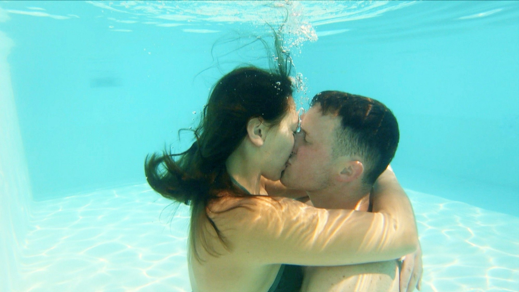 Ein junger Mann und eine junge Frau küssen sich unter Wasser in einem Swimmingpool.
