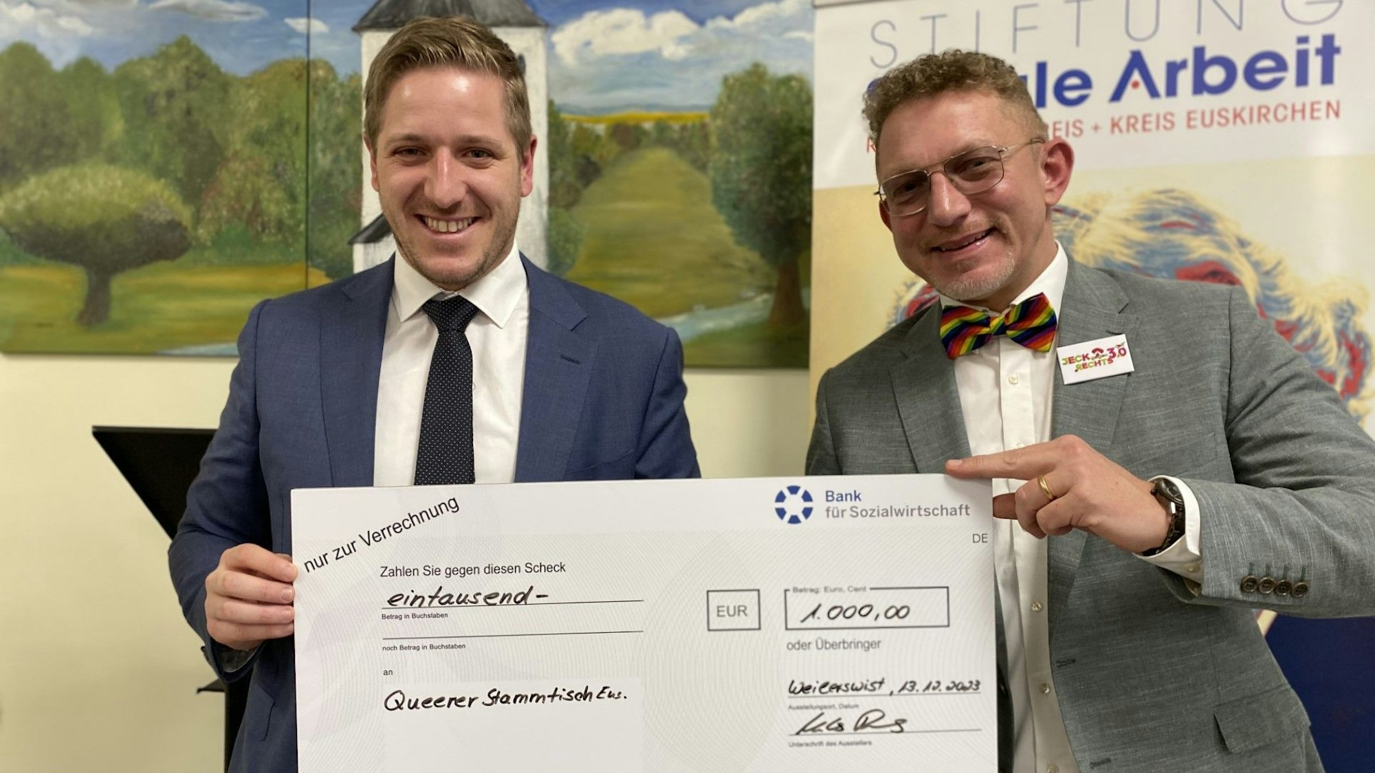 Markus Ramers überreicht Winfried Kubitza-Simons, Gründungsmitglied des Queeren Stammtischs einen Scheck über 1000 Euro.