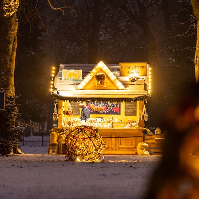 beleuchtete Holzhütte mit Verkaufstresen in einer Winterlandschaft