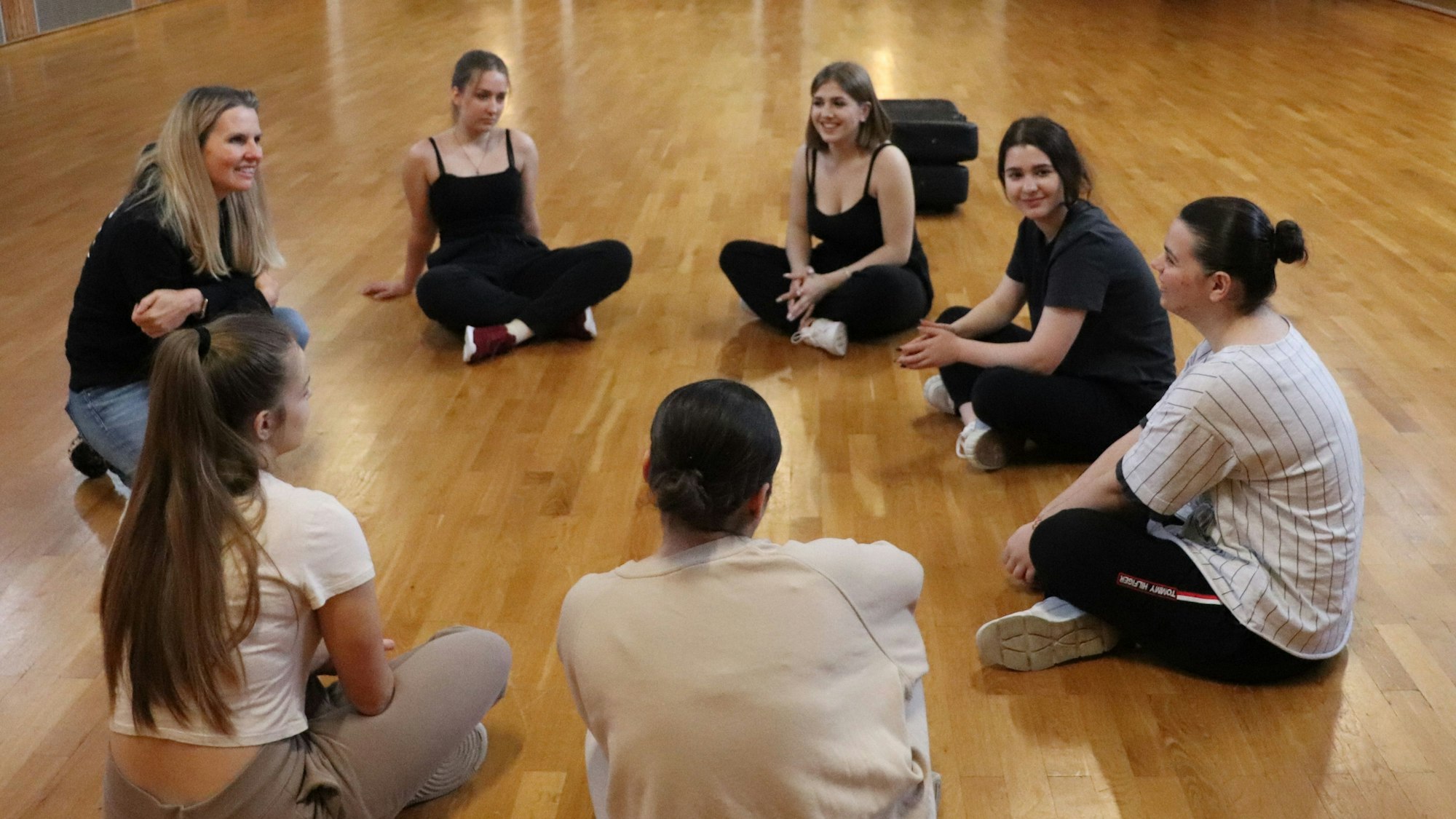 Jugendliche Teilnehmerinnen des Krav-Maga-Workshops sitzen auf dem Boden im Kreis.