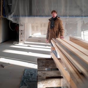 Das Bild zeigt Carsten Opitz hinter einem Stapel Holz, auf den er die linke Hand gelegt hat.
