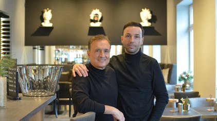 Zwei Männer stehen gemeinsam in einem Restaurant und schauen in die Kamera.
