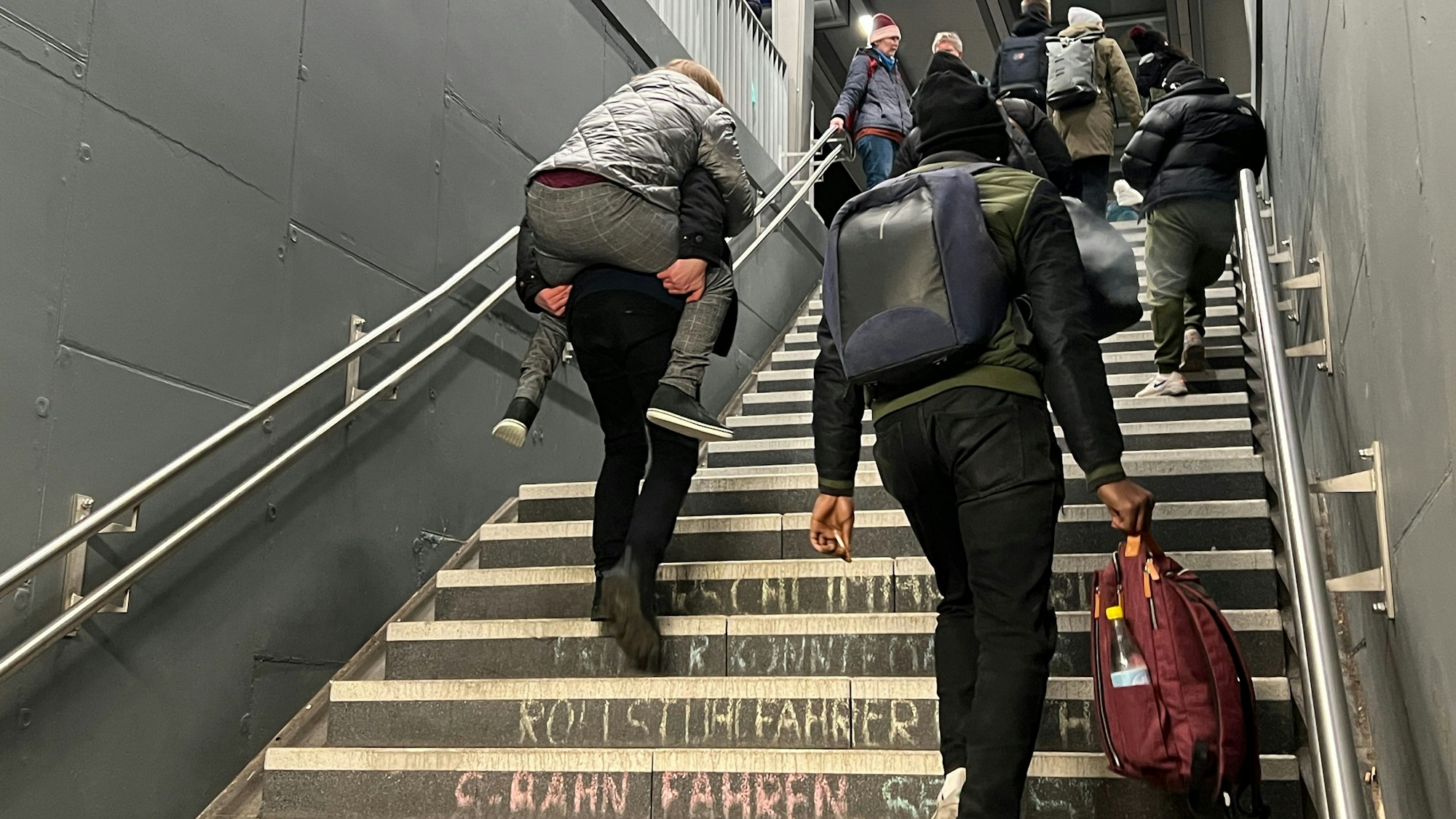 Ein Mann trägt eine Reisende im Bahnhof Mitte die Treppe hinauf, weil es immer noch keinen Fahrstuhl gibt.