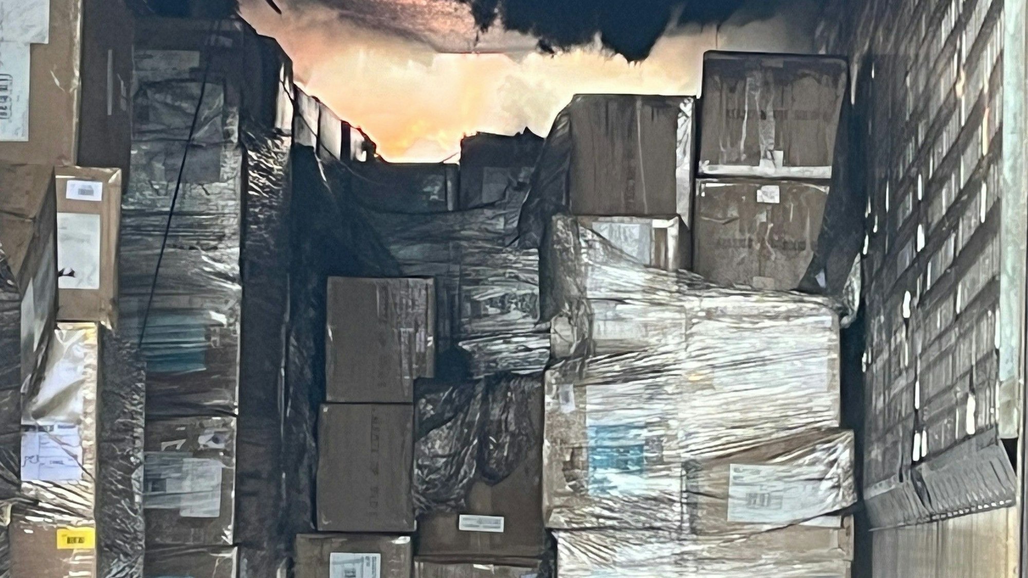 Blick in den Laderaum mit vielen angekokelten Kartons, im hinteren Teil lodern Flammen.