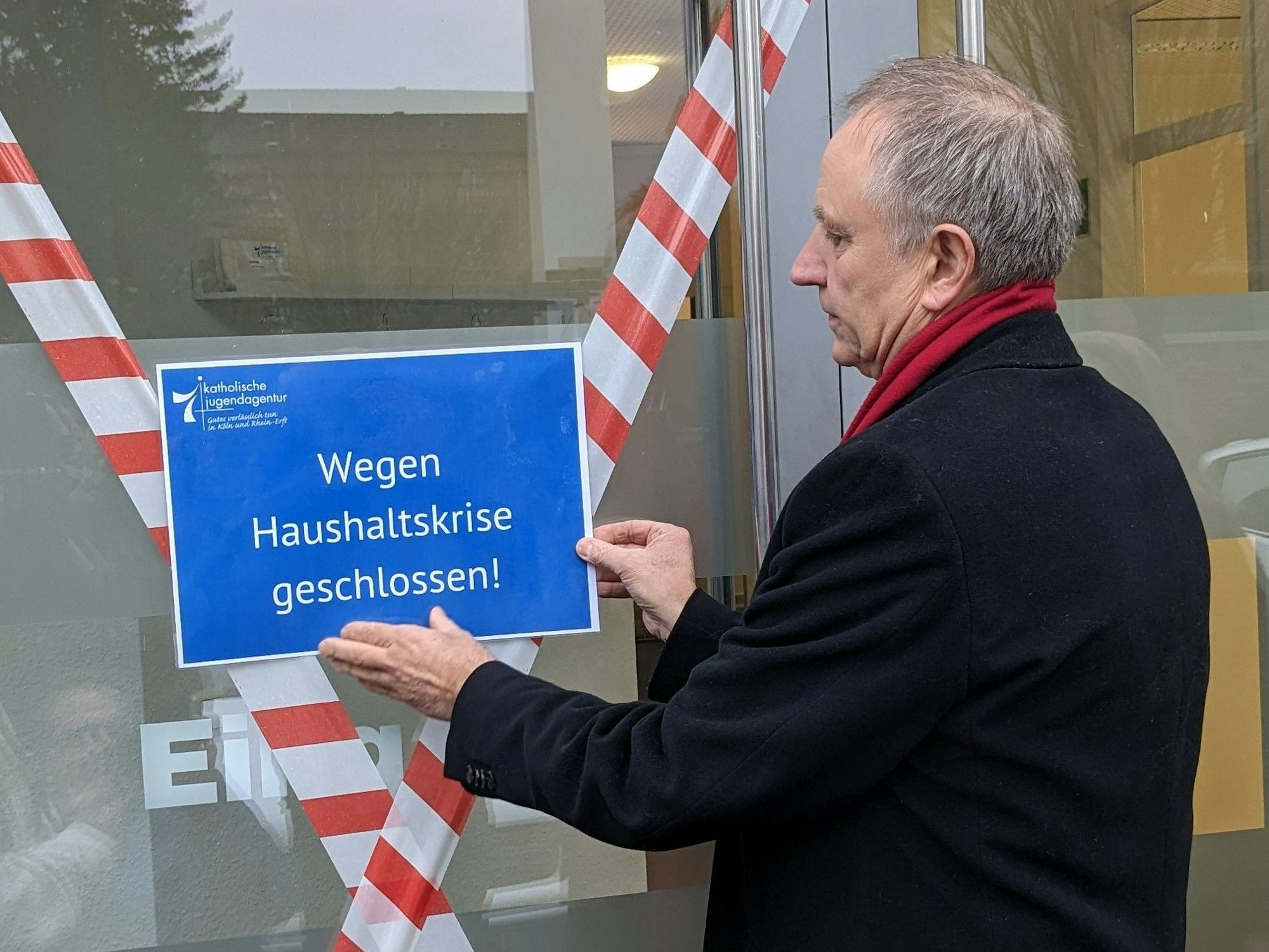 Georg Spitzley bringt ein Schild an, auf dem „Wegen Haushaltskrise geschlossen!“ steht.