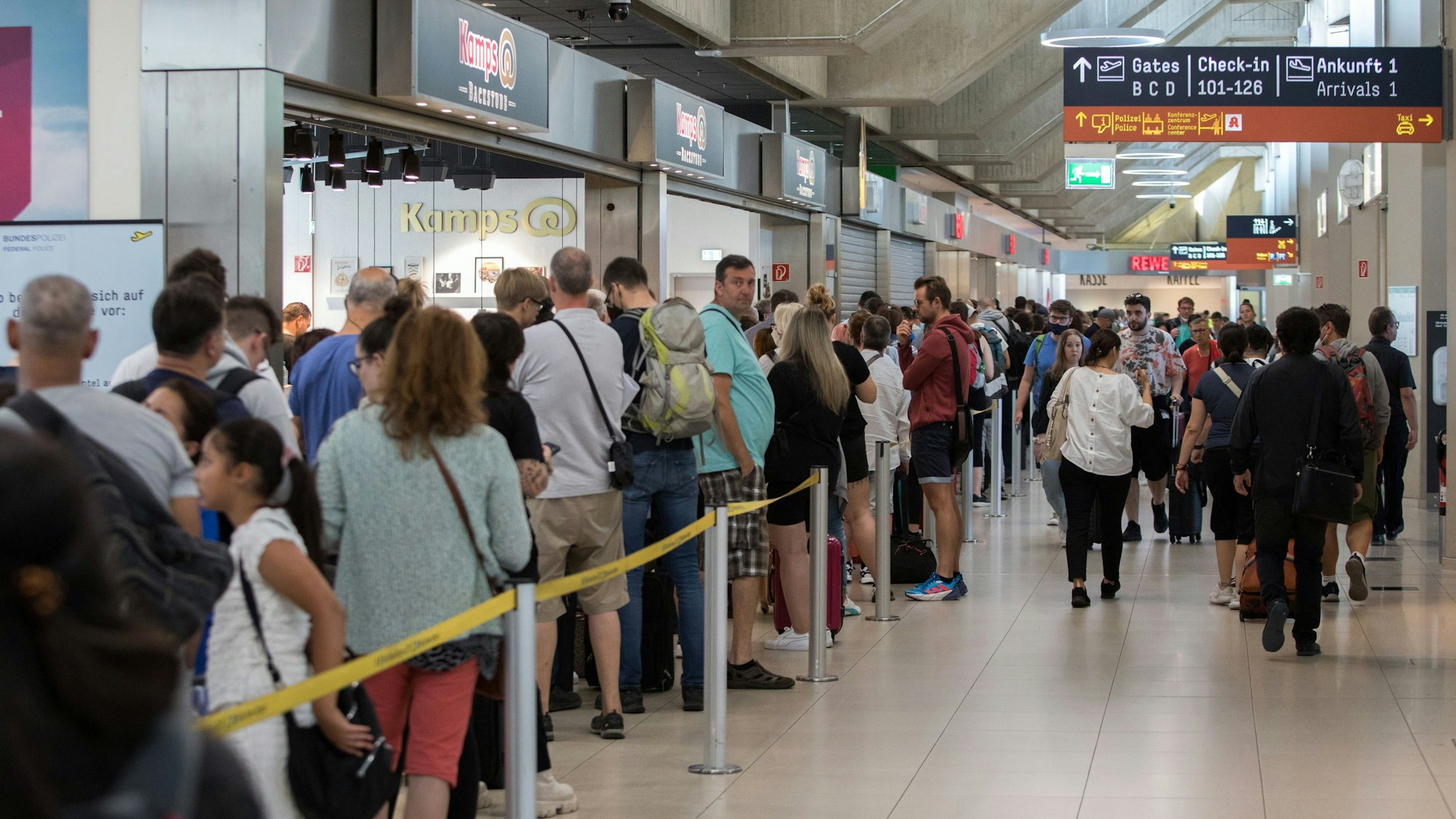 Diverse Menschen stehen am Flughafen Köln/Bonn in einer Warteschlange.
