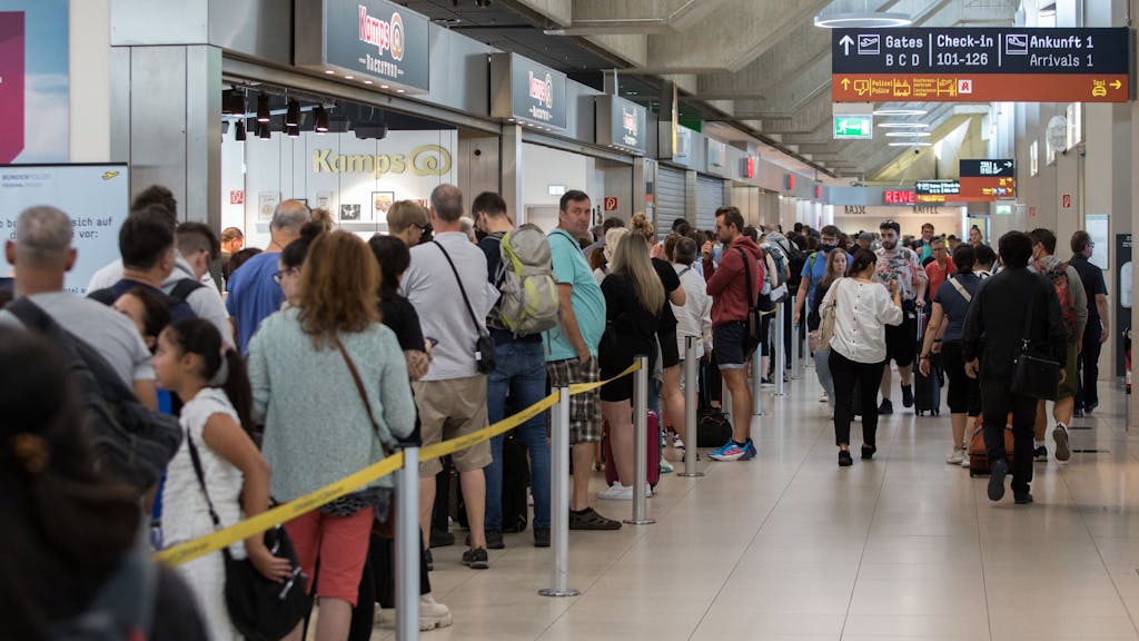 Diverse Menschen stehen am Flughafen Köln/Bonn in einer Warteschlange.