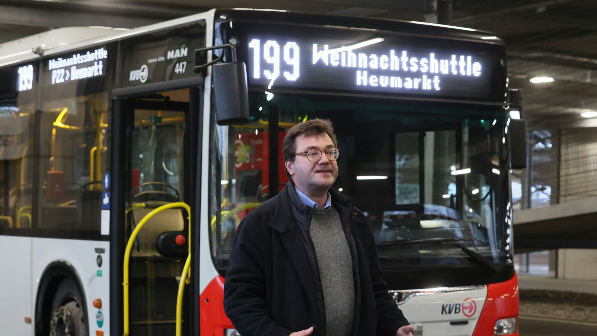 KVB-Sprecher Stephan Anemüller steht vor einem Bus, auf dem „Weihnachtsmarktshuttle Heumarkt“ steht und gestikuliert.