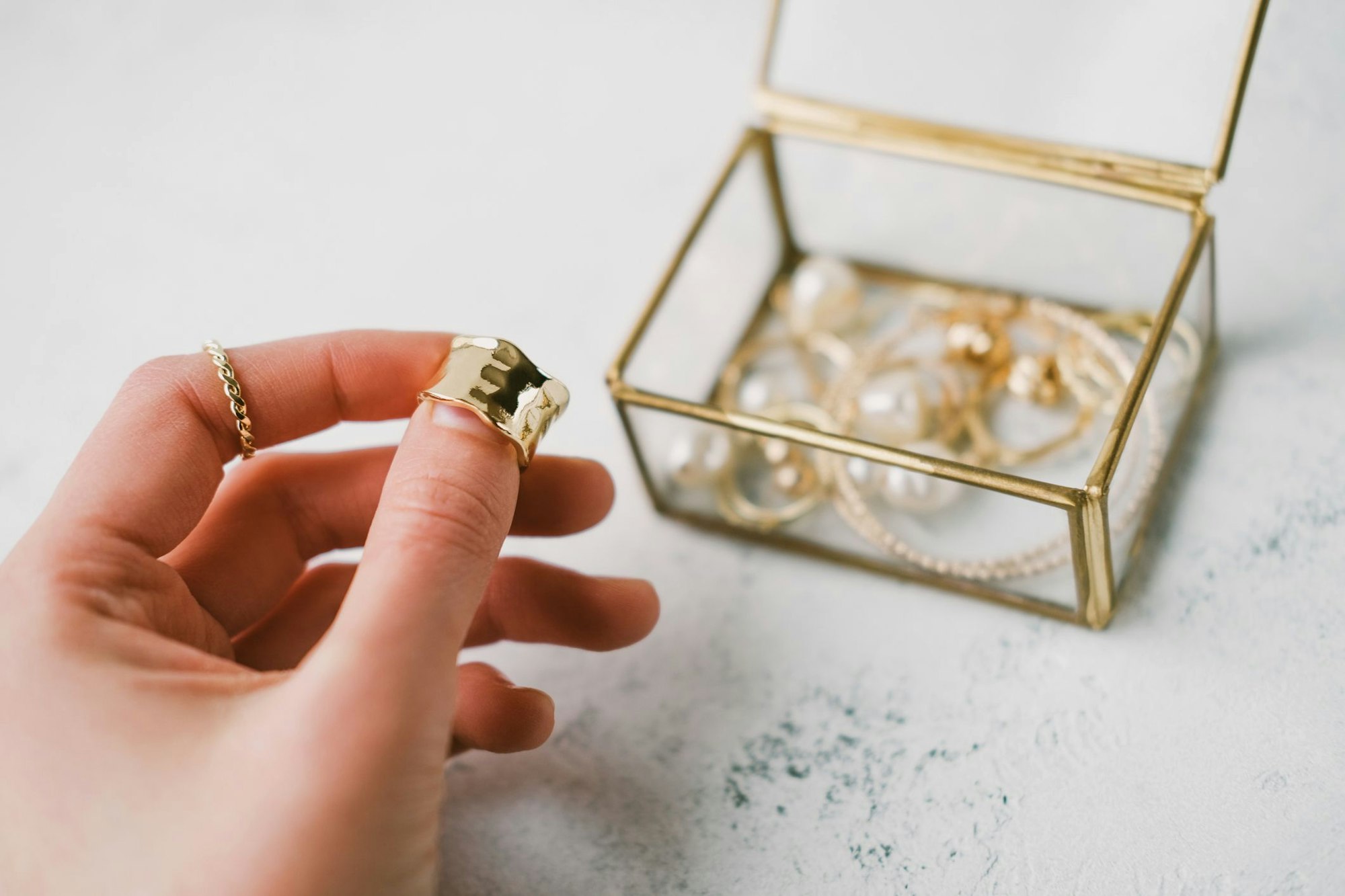 A woman's hand holds a gold ring on the background of a transparent jewelry box with accessories