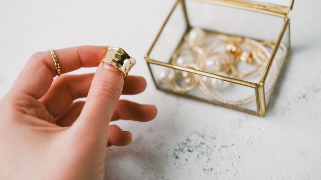 A woman's hand holds a gold ring on the background of a transparent jewelry box with accessories