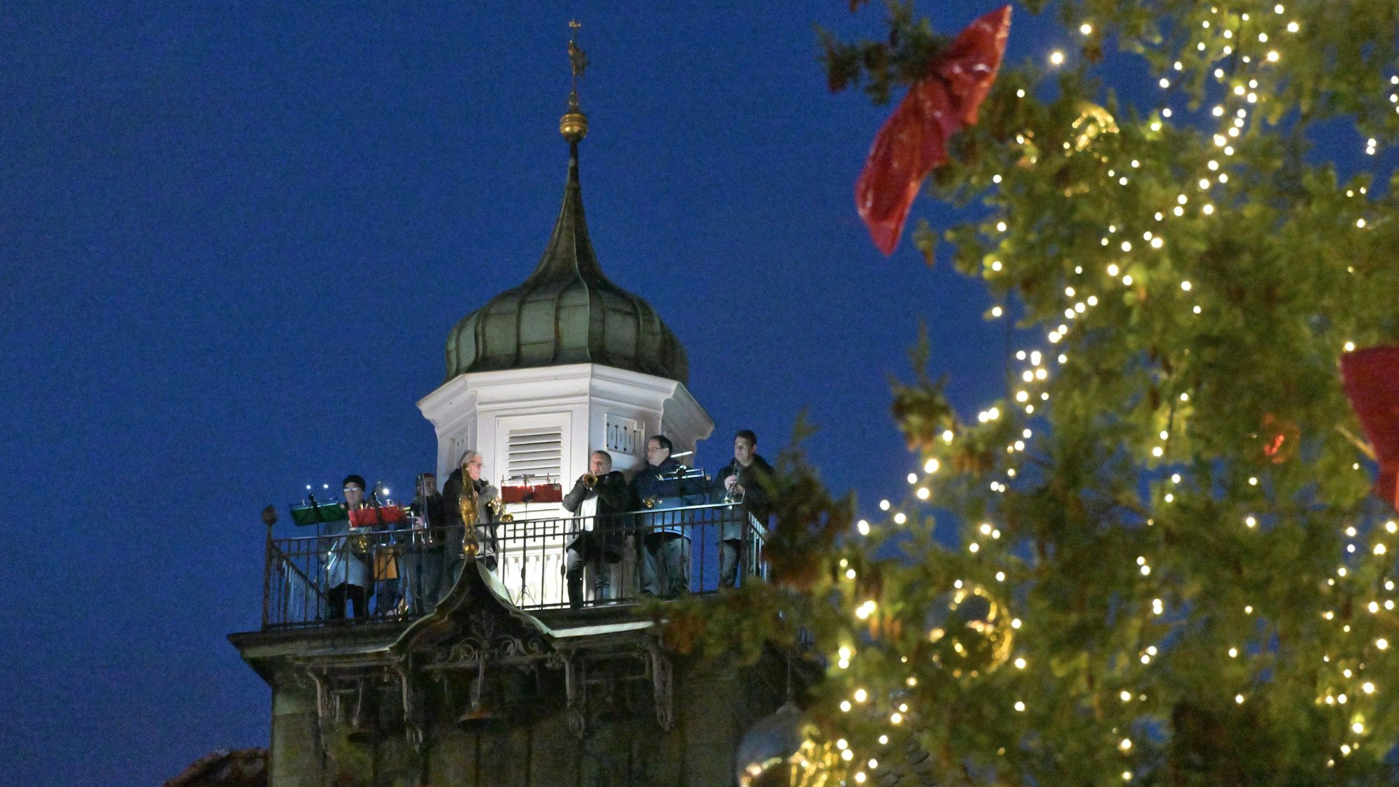Musiker spielen auf dem Turm des Bergisch Gladbacher Rathauses, im Vordergrund ist ein Weihnachtsbaum zu sehen.