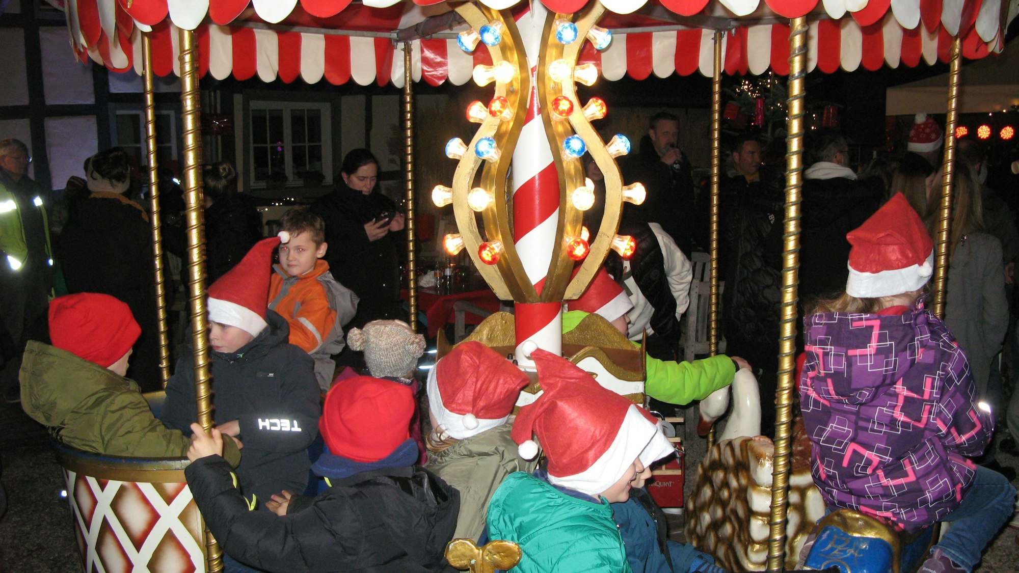 Kinder mit Nikolausmützen auf einem kleinen Karussell.