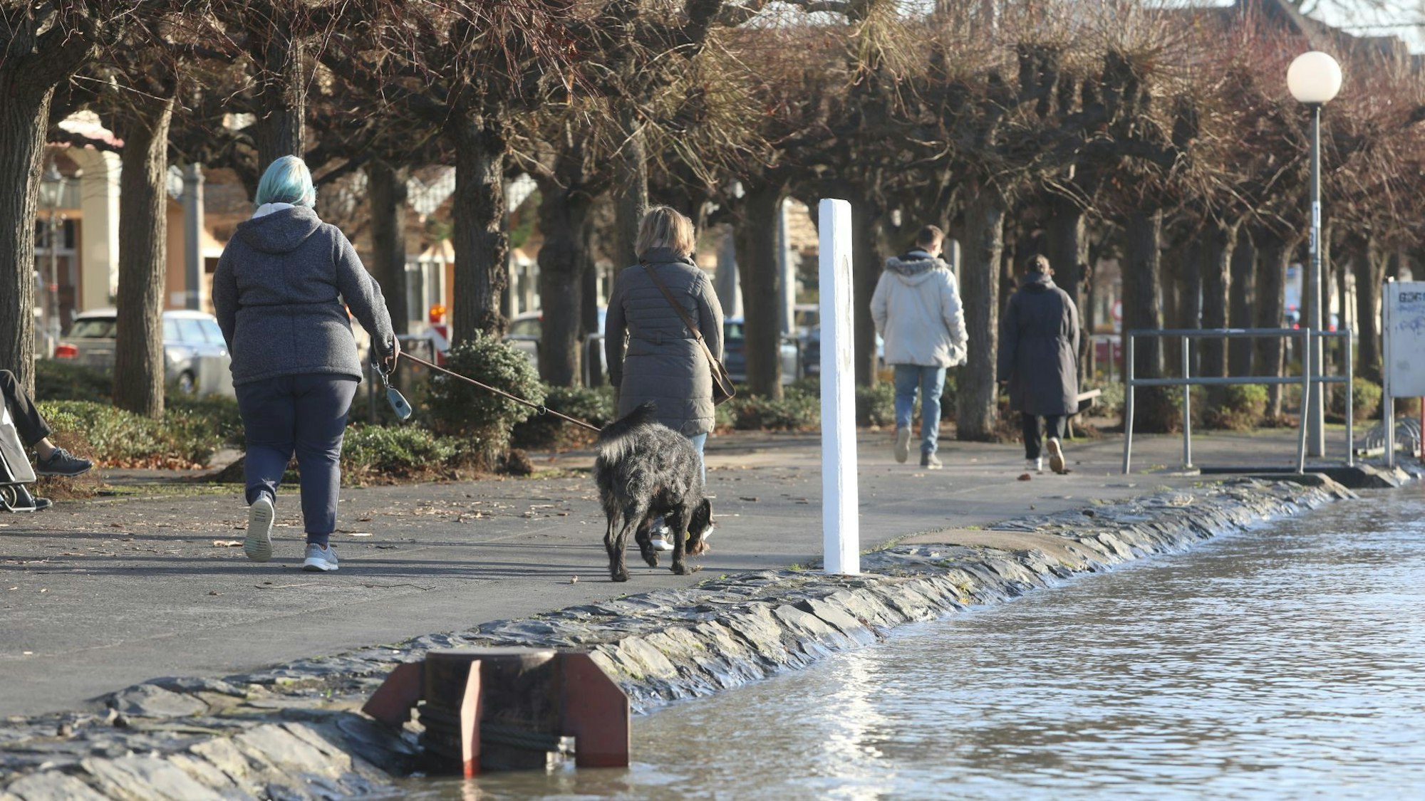 Spaziergänger auf einer Uferpromenade. Das Wasser steht nur wenige Zentimeter unterhalb des Weges.
