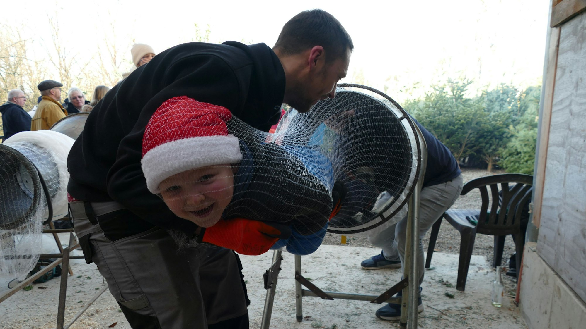 Ein Kind mit Nikolausmütze wird in ein Tannenbaumnetz gepackt.