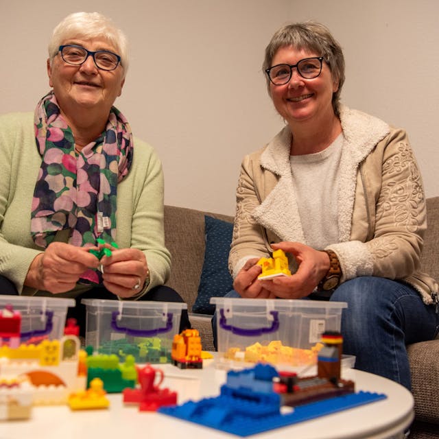 Das Bild zeigt Anita Sauer (l.) und Vera Schröder auf einem Sofa sitzend. Vor ihnen steht auf einem Tisch Lego-Spielzeug.