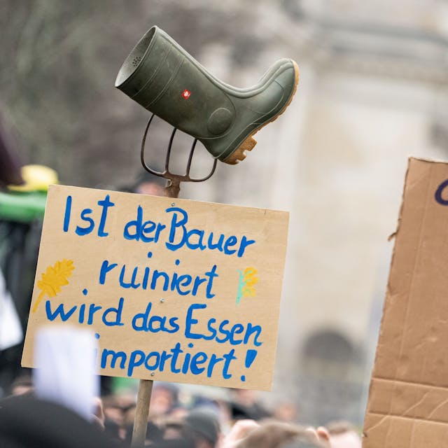 Auf einer Demonstration des Deutschen Bauernverbandes unter dem Motto „Zu viel ist zu viel! Jetzt ist Schluss!“ vor dem Brandenburger Tor in Berlin hält jemand ein Schild mit der Aufschrift „Ist der Bauer ruiniert, wird das Essen importiert“, mit eine Mistgabel und einem Gummistiefel hoch. Foto: Fabian Sommer/dpa +++ dpa-Bildfunk +++