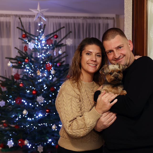 Daniela und Thomas Marschalleck mit ihrem kleinen Hund auf dem Arm vor dem Weihnachtsbaum