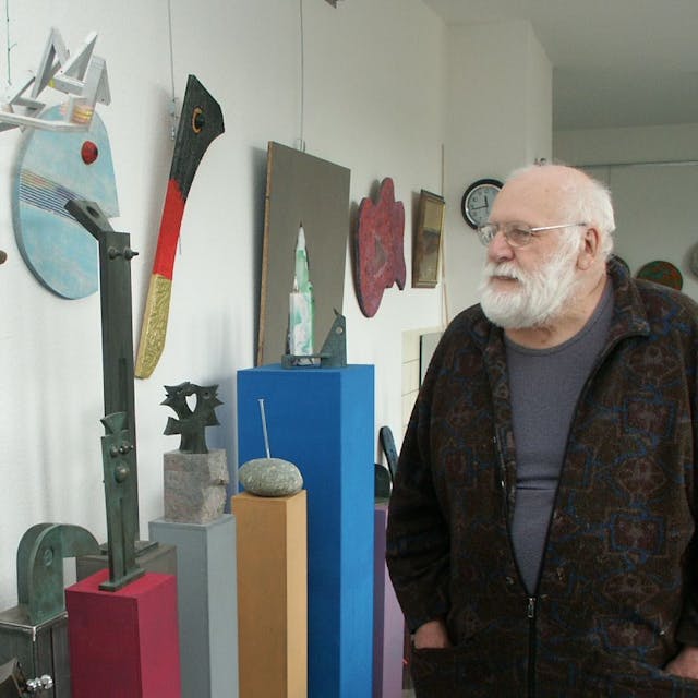 Ein alter Mann mit Bart und Brille schaut sich Kunstwerke an.