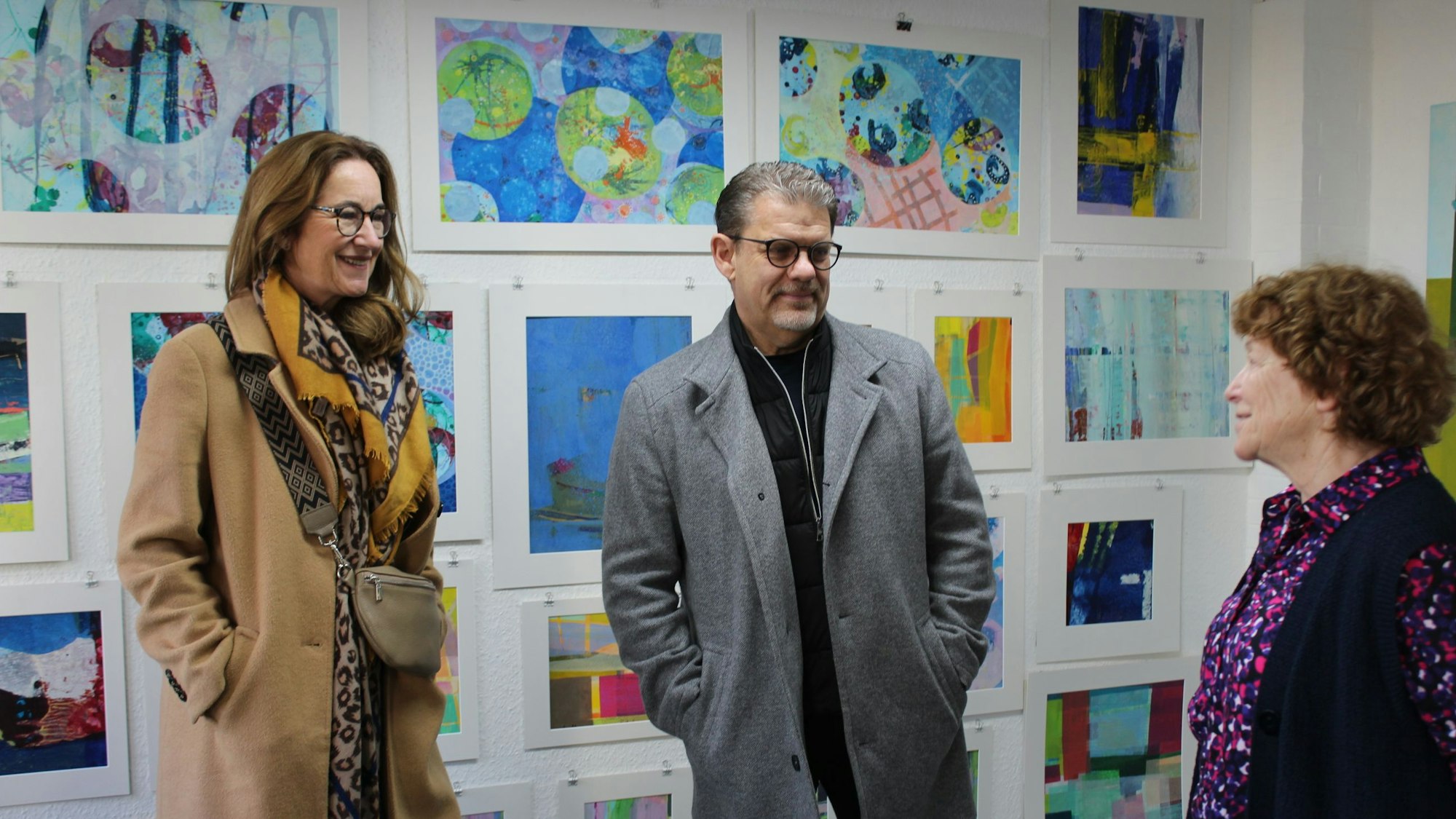 Drei Menschen stehen vor einer Wand mit Kunstwerken.