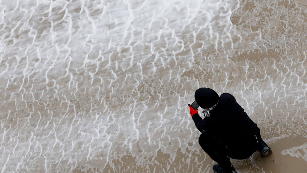 Eine Frau fotografiert mit ihrem Smartphone das von Orkanböen aufgepeitschte Wasser der Nordsee.