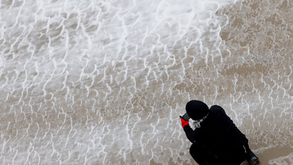 Eine Frau fotografiert mit ihrem Smartphone das von Orkanböen aufgepeitschte Wasser der Nordsee.