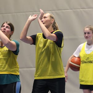 Julia Reuß hält einen Basketball in den Händen, neben ihr steht eine Basketballerin der ErftBaskets und erklärt ihr die richtige Wurftechnik.