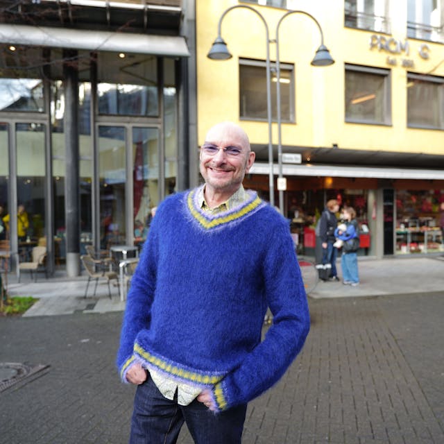 Schauspieler Ralph Morgenstern mit Glatze, leicht getönter Brille und knallig blauem Pullover auf der Breitestraße.