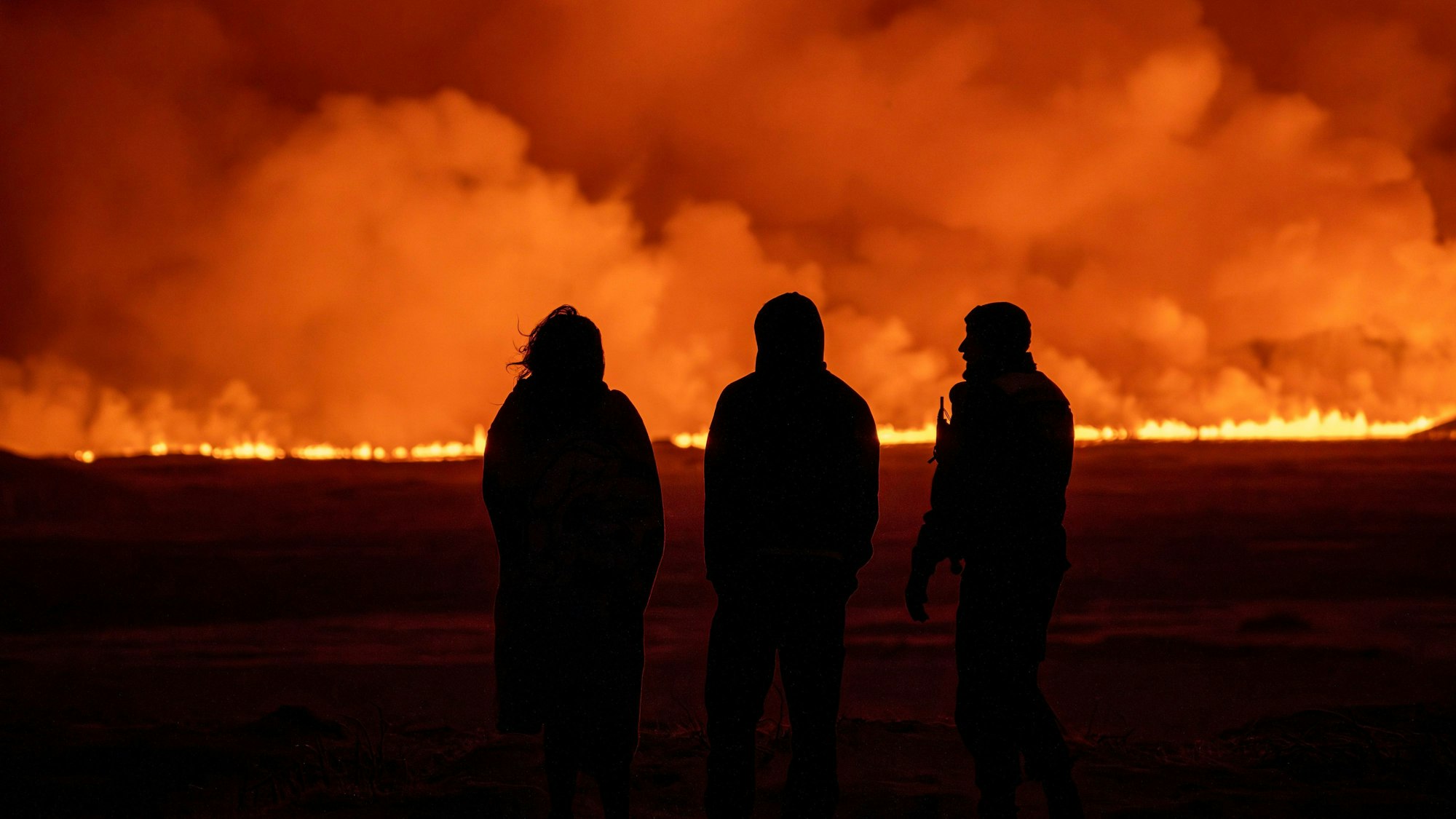 Vulkanausbruch auf Island: Drei Personen beobachten das Feuer und den orangen Rauch.