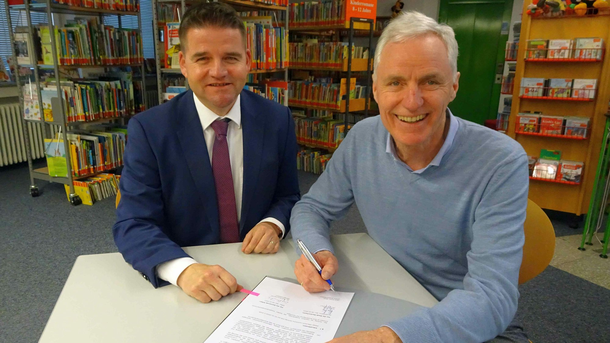Bürgermeister Holger Jung (links) und sein Alfterer Kollege Dr. Rolf Schumacher unterzeichnen den Vertrag in den Räumen der Meckenheimer Bücherei.