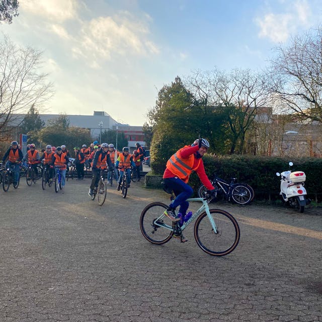 Eine Gruppe von Fahrradfahrern mit orangen Warnwesten startet vor dem Freiherr-vom-Stein Gymnasium.