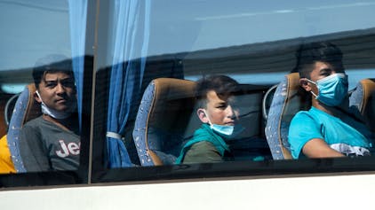 Junge Flüchtlinge, teilweise mit Mundschutz, sitzen in einem Bus am Flughafen Hannover.