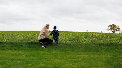 Julia Trienens blickt mit ihrem Kind auf eine Wiese in der Umgebung ihres Wohnhauses.