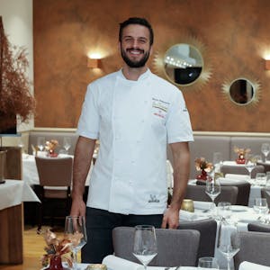Gastronom Malon Rademacher in weißem Koch-Hemd zwischen den Tischen seines Restaurants.