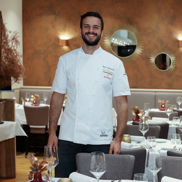 Gastronom Malon Rademacher in weißem Koch-Hemd zwischen den Tischen seines Restaurants.